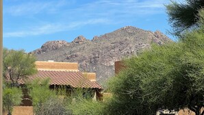A building with a red-tiled roof, surrounded by greenery and a mountainous backdrop. - Foothills 2-bedroom condo in welcoming Tucson with AC and fitness room (Tucson)
