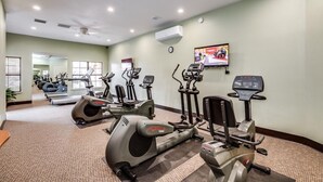 A gym with various cardio machines, a ceiling fan, and a TV on the wall. - Foothills 2-bedroom condo in welcoming Tucson with AC and fitness room (Tucson)