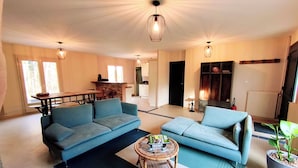 Een ruime woonkamer met een blauwe zithoek, een klein rond tafeltje en een potplant.
