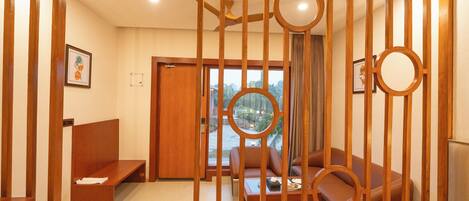A modern hotel room with a wooden partition, a sofa, a coffee table, and a view of the cityscape.