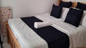 A neatly made bed with white and navy bedding, a wooden headboard, and a single pillow. - The Greenzone Apartments Thindigua (Kiambu)