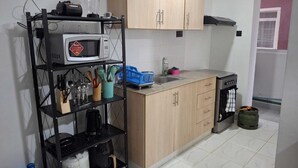 A compact kitchen with a microwave, sink, and stove. There is a shelf with utensils and a blue basket. - The Greenzone Apartments Thindigua (Kiambu)