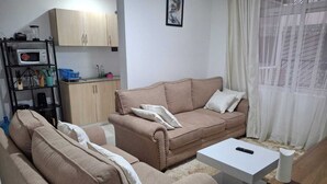 A living room with a beige sofa, a coffee table, and a kitchen area with a microwave and cabinets. - The Greenzone Apartments Thindigua (Kiambu)