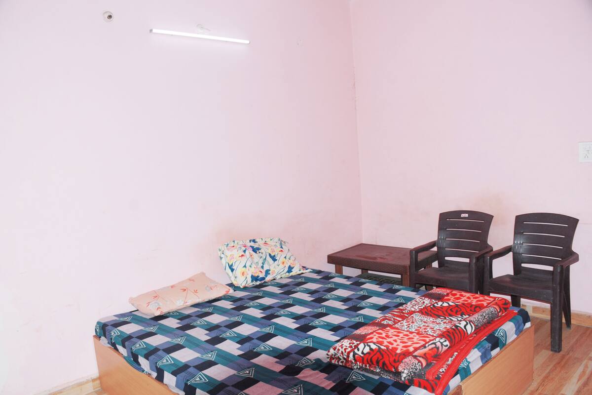 A bedroom with a bed, two chairs, a small table, and a wall socket.