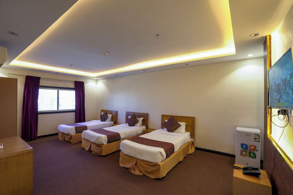 A hotel room with two beds, a desk, a refrigerator, and a window with curtains.