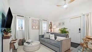 Un salon avec un canapé gris, une table basse ronde, un téléviseur et un ventilateur de plafond.