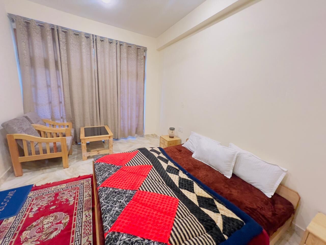 Un dormitorio con cama, una silla de madera, una mesita y una ventana con cortinas.