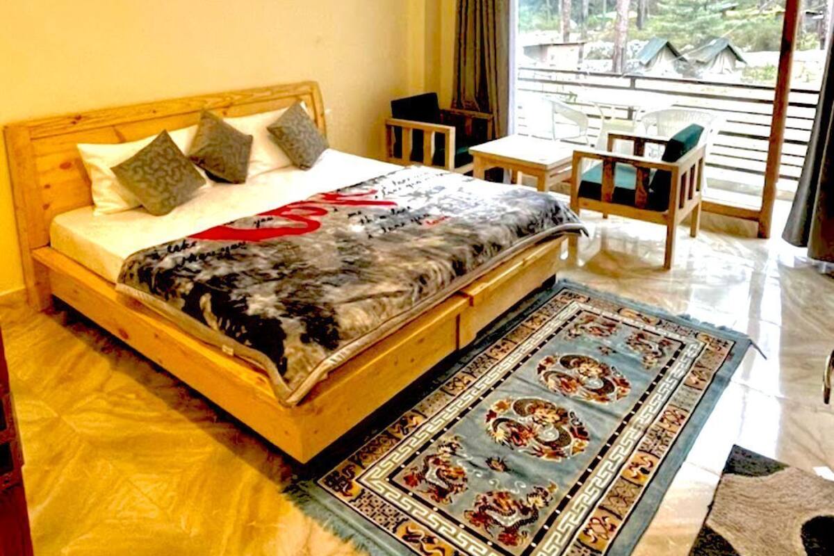 A bedroom with a bed, a desk, and a view of a forest through large windows.