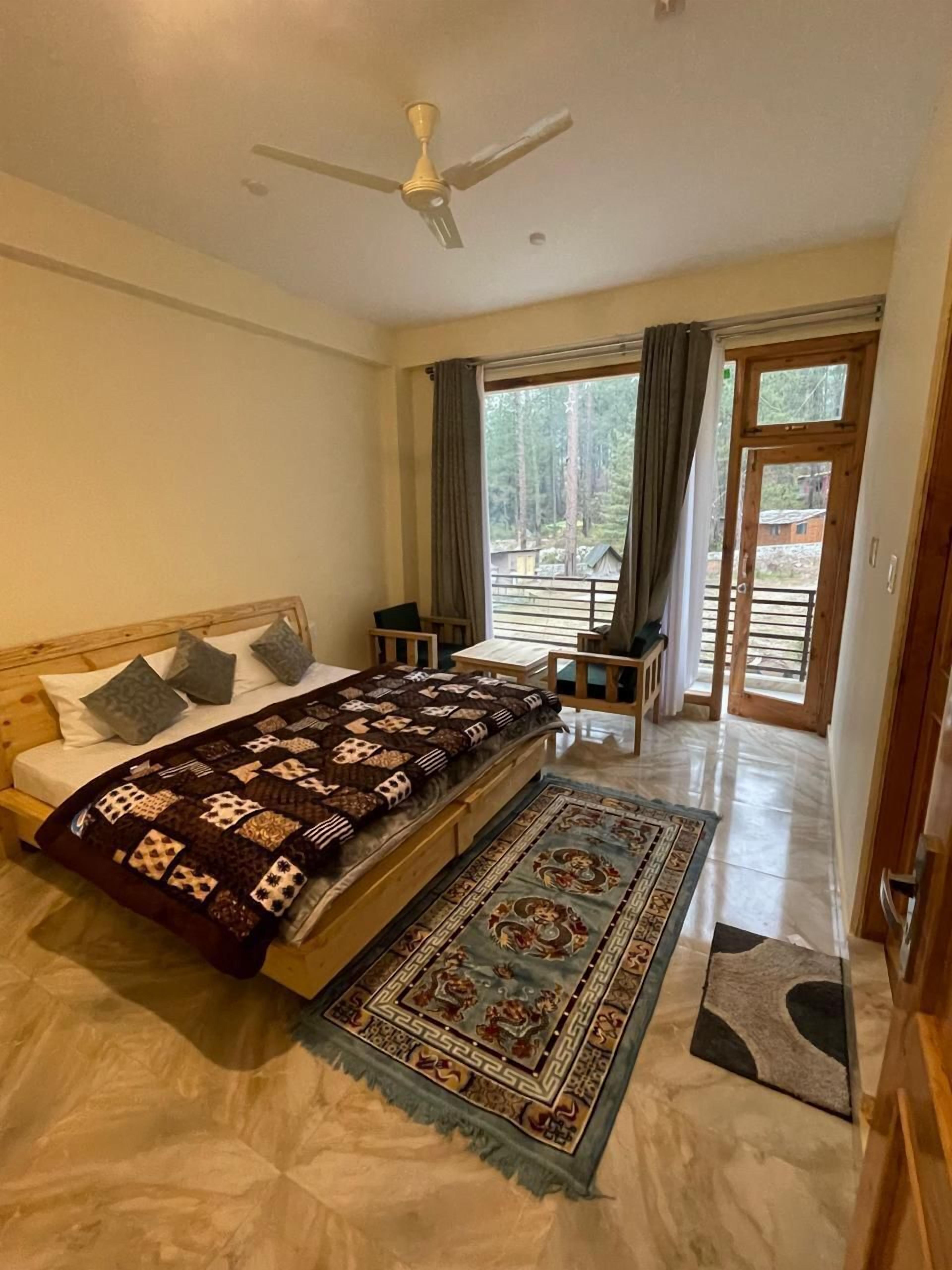 Un dormitorio con cama, escritorio, silla, ventilador de techo y vistas al exterior.