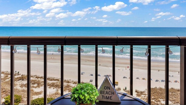 A balcony with a view of the beach, a sign indicating 'ON BEACH TIME', and a plant in the foreground. - Beach Colony Oceanfront w/ Indoor & Outdoor Pools (Myrtle Beach)