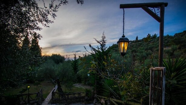 A rustic outdoor pathway leading to a wooden gate, surrounded by lush greenery and a hanging lantern. - Gigi Star Tatiana Luxury Apartment (Zakynthos)
