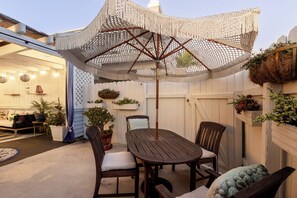 An outdoor patio with a wooden table and chairs, a woven umbrella, and potted plants. - Enchanting Ocean View Townhome | Walk to Beach, Dining & More (Encinitas)