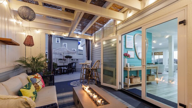 A cozy outdoor seating area with a fire feature, wicker furniture, and a view into the adjacent room. - Enchanting Ocean View Townhome | Walk to Beach, Dining & More (Encinitas)