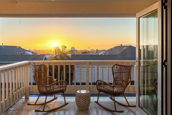 A balcony with two rocking chairs and a small table, overlooking a sunset view of a residential area. - Enchanting Ocean View Townhome | Walk to Beach, Dining & More (Encinitas)
