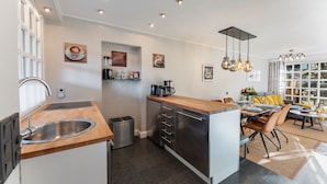 A modern kitchen with a central island, stainless steel appliances, and a dining area with a sofa and table. - Vacation home "Hüs Swarte Wall" (Kampen (Sylt))