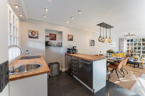 A modern kitchen with a central island, stainless steel appliances, and a dining area with a sofa and table. - Vacation home "Hüs Swarte Wall" (Kampen (Sylt))