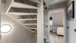 A modern interior with a spiral staircase, a minimalist design, and a view into a bedroom with a bed and a nightstand. - Vacation home "Hüs Swarte Wall" (Kampen (Sylt))