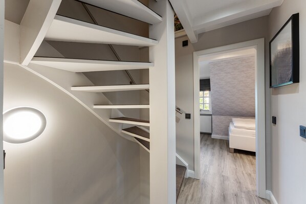 A modern interior with a spiral staircase, a minimalist design, and a view into a bedroom with a bed and a nightstand. - Vacation home "Hüs Swarte Wall" (Kampen (Sylt))