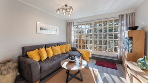 A modern living room with a grey sofa, yellow cushions, a round coffee table, and a large window with curtains. - Vacation home "Hüs Swarte Wall" (Kampen (Sylt))