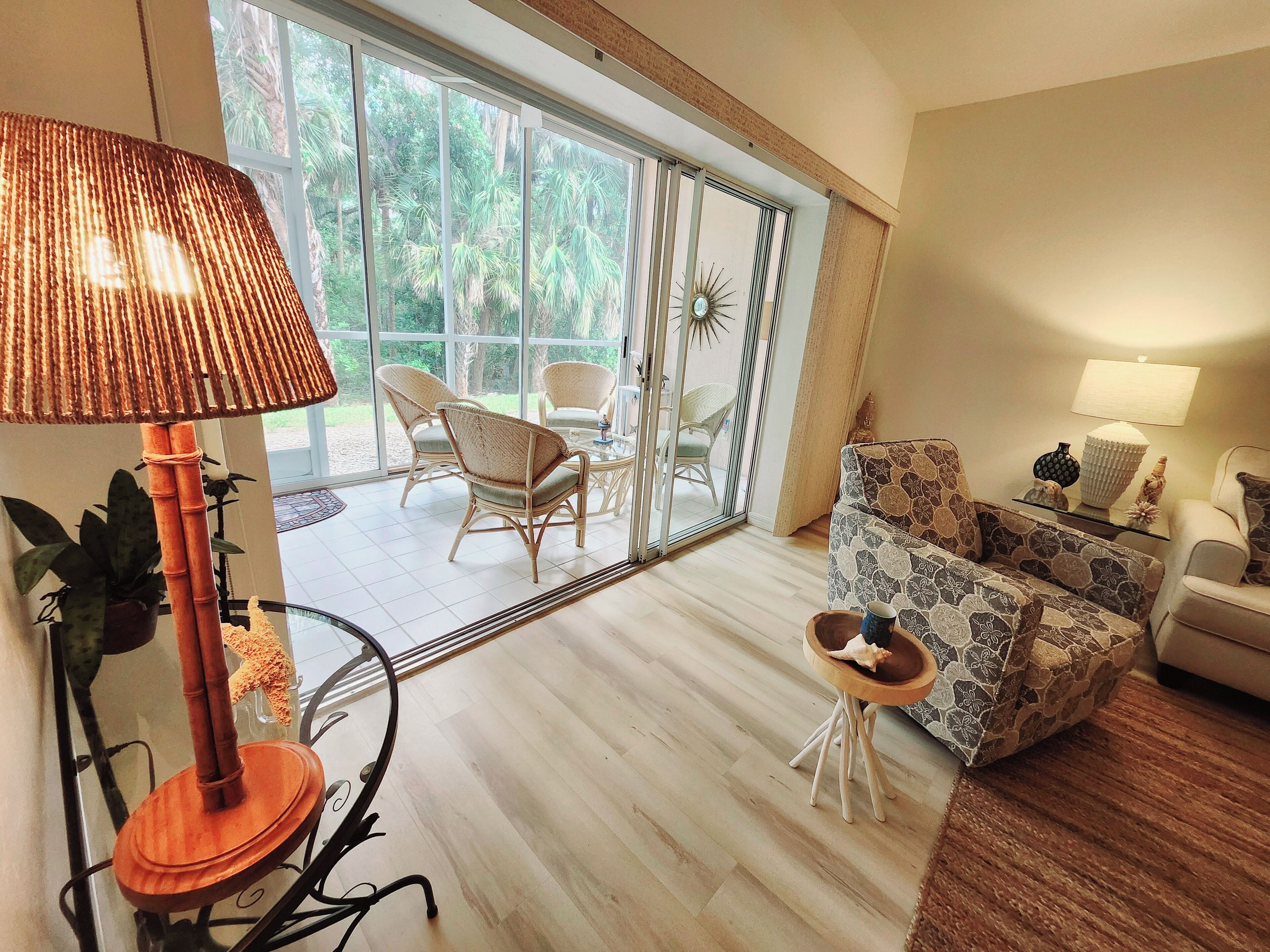 A spacious living room with a large sliding glass door leading to a patio area, a round table with chairs, and a patterned sofa.