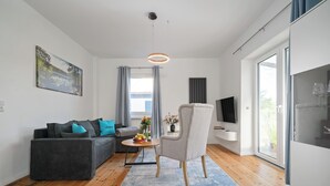 Una sala de estar moderna con un sofá gris, una mesa de centro redonda, un sillón blanco y un televisor montado en la pared.