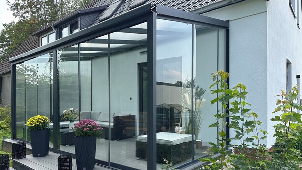 Un patio moderno con paredes de vidrio, mobiliario exterior y plantas en macetas.