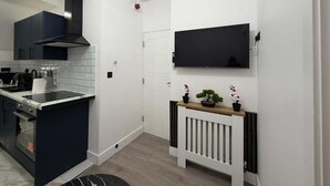 A modern kitchen with a black stove, white tiles, and a black TV mounted on the wall. - Cardiff Central Gem - 2 Bed Apartment (Cardiff)