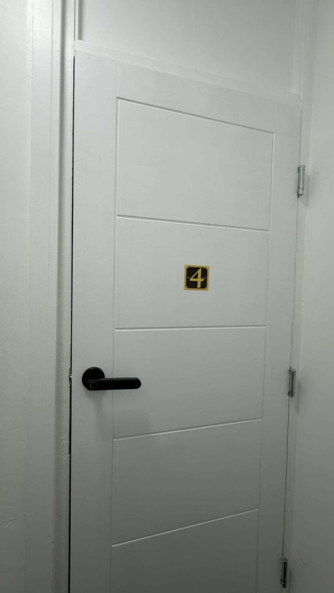 Une porte blanche avec une poignée noire et une petite plaque portant le chiffre « 4 », en noir et or.