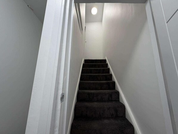 A narrow stairway with carpeted steps leading to a landing with a ceiling light. - Cardiff Central Gem - 2 Bed Apartment (Cardiff)