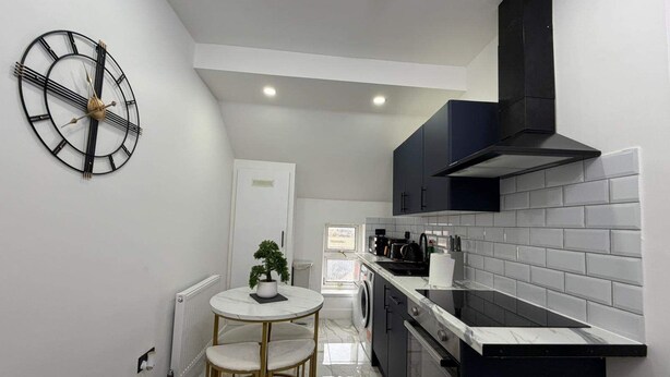 A modern kitchen with a round table, a clock, and a black stove. - Cardiff Central Gem - 2 Bed Apartment (Cardiff)
