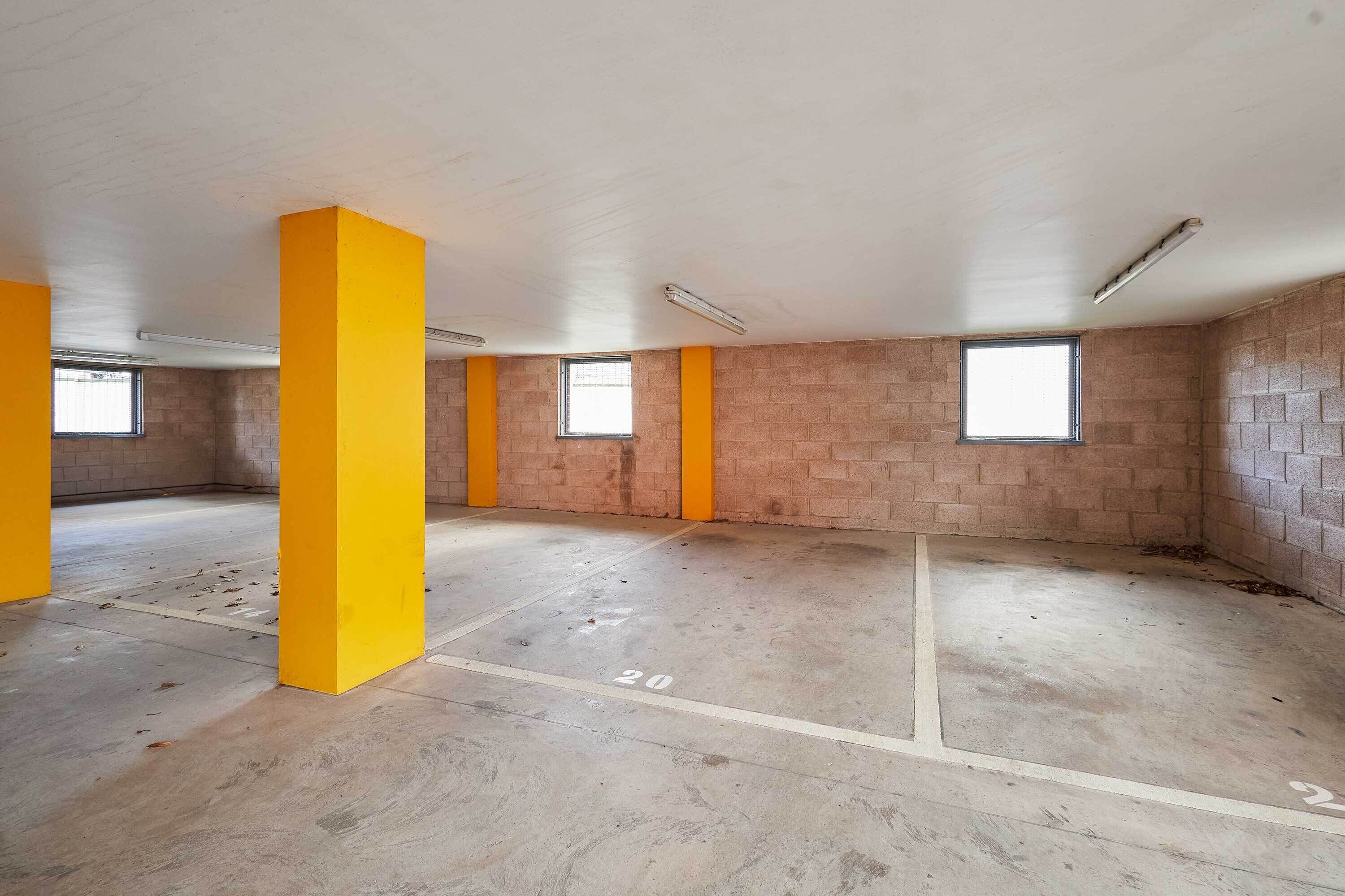 A vacant room with brick walls, yellow pillars, and a concrete floor marked with parking lines.