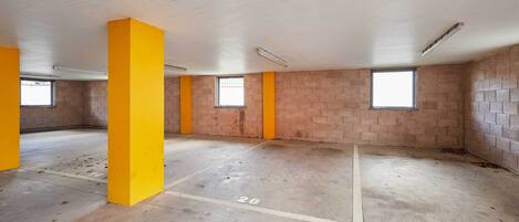 A vacant room with brick walls, yellow pillars, and a concrete floor marked with parking lines.
