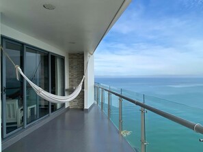 Ein Balkon mit einer Hängematte, Glastüren und Blick aufs Meer.