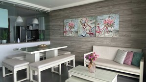 A modern living room with a sofa, two benches, a coffee table, and a dining area with a glass-top table. - w Amazing 3BR w Ocean View in Marbella (Cartagena)