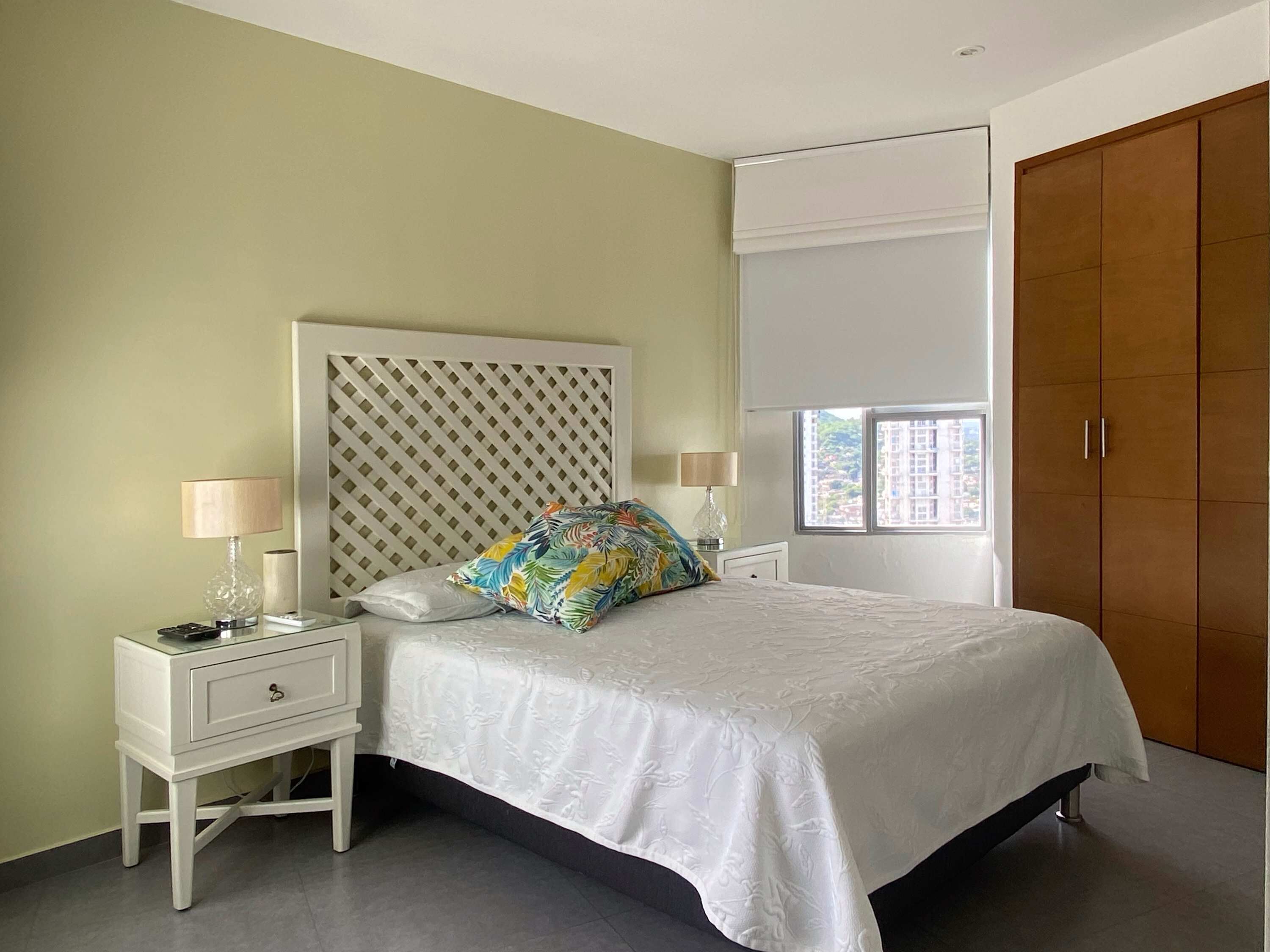 A bedroom with a bed, two bedside tables, a nightstand, a window, and a wardrobe.
