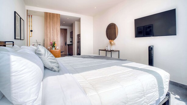 Een moderne slaapkamer met een groot bed, een nachtkastje met een vaas, een spiegel en een flatscreen televisie aan de muur.