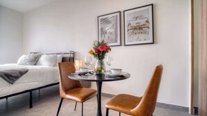 Een hotelkamer met een bed, een ronde eettafel met twee stoelen, een vaas met bloemen en twee ingelijste foto's aan de muur.
