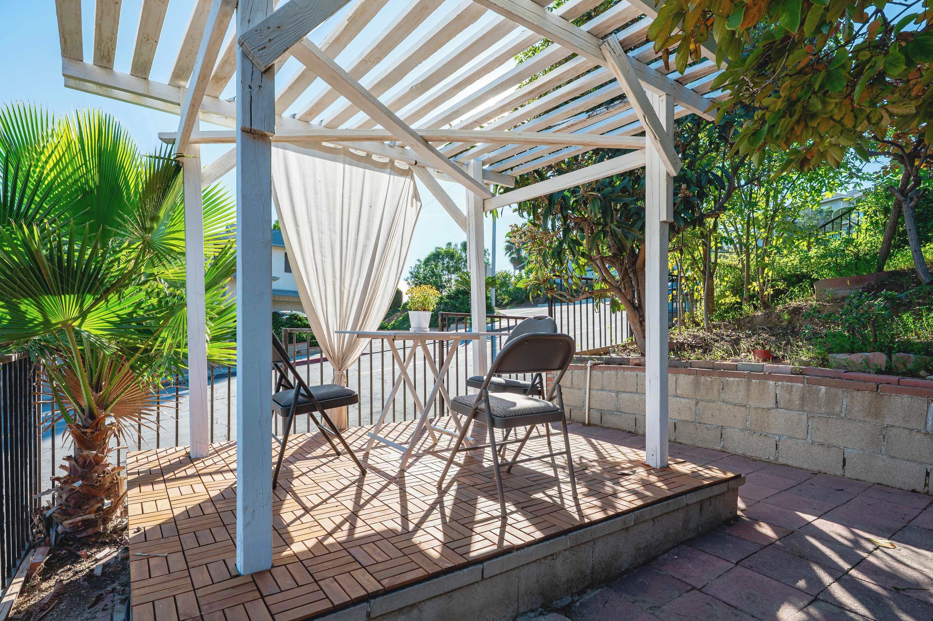 A covered patio area with a pergola, two chairs, and a table.