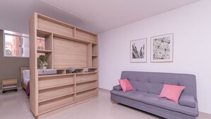 Ett modernt vardagsrum med en grå soffa, en hylla i trä och två inramade konstverk med blommotiv på väggen.
