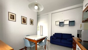 Ein kompakter Wohnraum mit Esstisch und Stühlen, einem blauen Sofa, einer Küchenzeile mit Mikrowelle und gerahmten Bildern an der Wand.