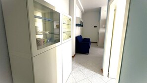 Ein schmaler Flur mit einer Küchenzeile links, einem blauen Sofa in der Mitte und einer Tür, die in einen weiteren Raum führt, rechts.