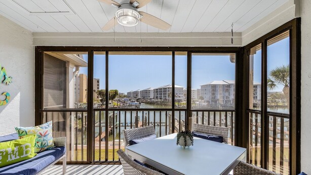 A balcony with a table and seating, overlooking a marina and buildings. - Estero Island Yacht & Racquet Club 224 1 Bedroom Condo (Fort Myers Beach)