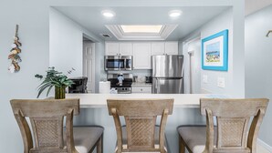 A modern kitchen with white cabinets, stainless steel appliances, and a central island with bar stools. - Estero Island Yacht & Racquet Club 224 1 Bedroom Condo (Fort Myers Beach)