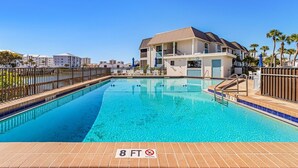 A swimming pool with a 7 ft 6 in depth sign, surrounded by a fence, and adjacent to a building with balconies. - Estero Island Yacht & Racquet Club 224 1 Bedroom Condo (Fort Myers Beach)