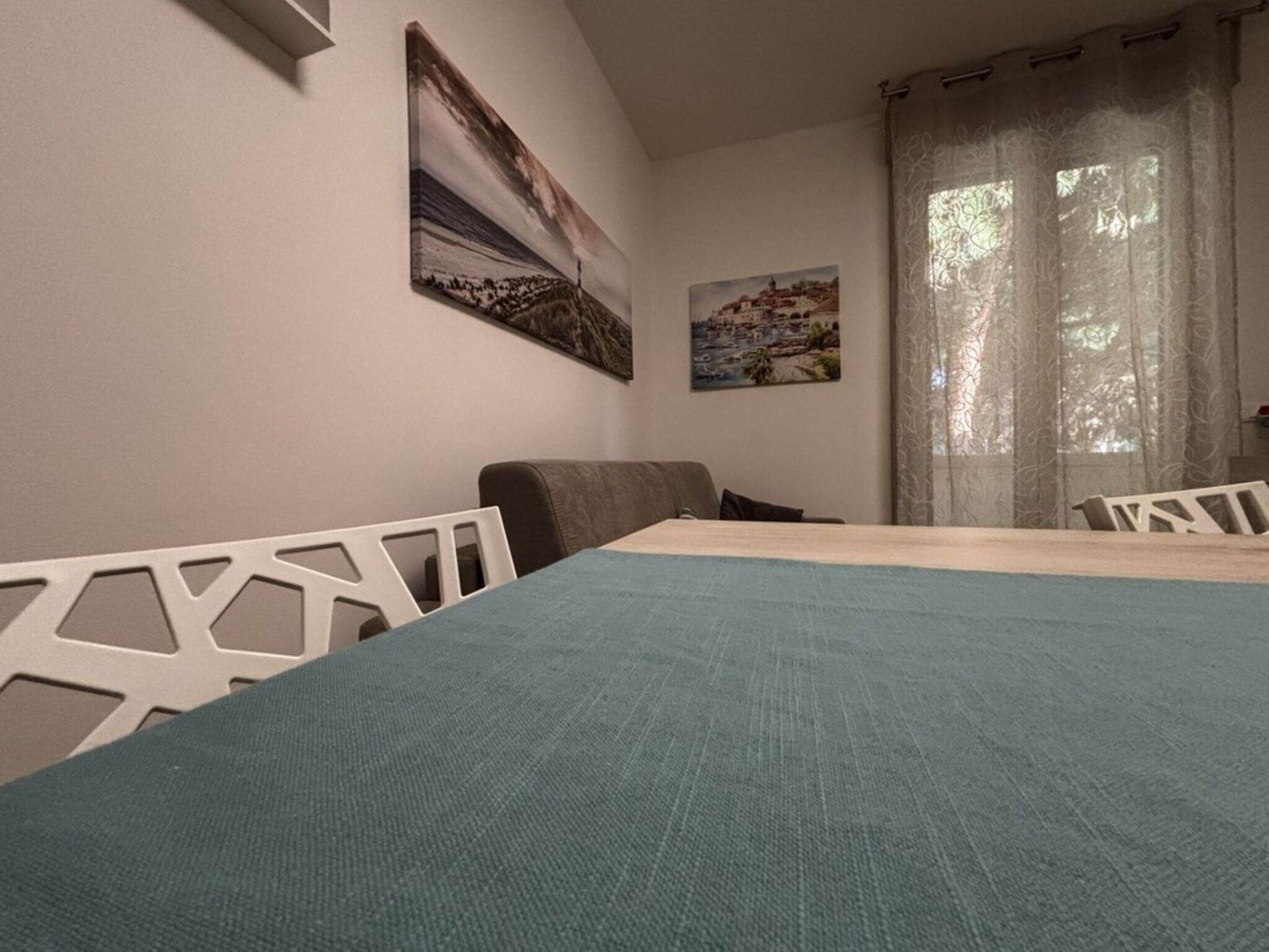A bedroom with a bed, two chairs, a window with curtains, and two paintings on the wall.