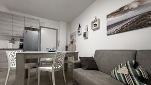 Ein modernes Wohnzimmer mit grauem Sofa, einem Esstisch mit Stühlen und einer Küche im Hintergrund.