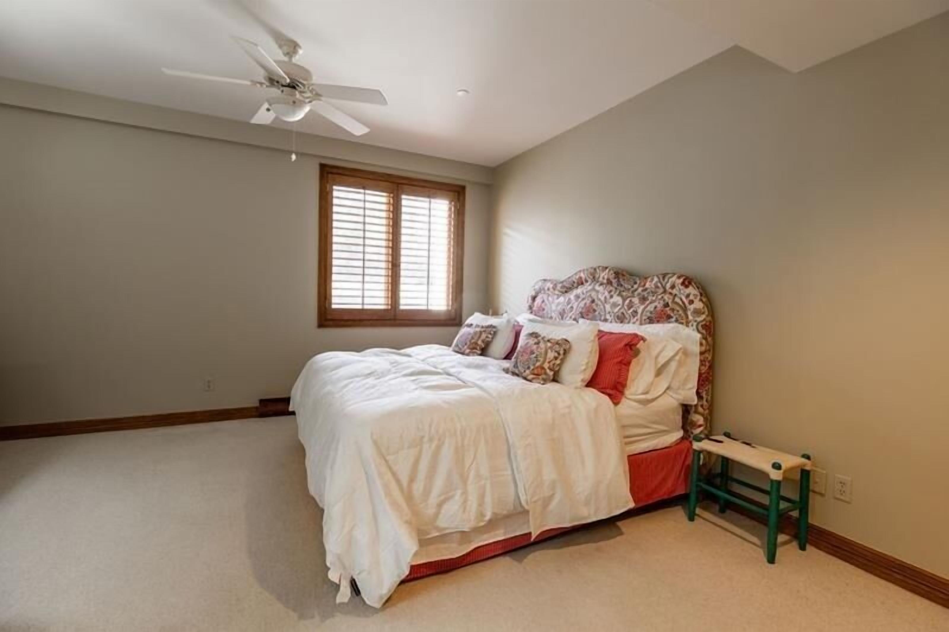 A bedroom with a bed, a ceiling fan, a window, and a small bench.