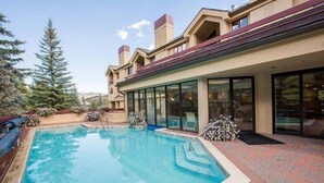 A swimming pool with a brick deck, surrounded by a building with large windows and a flat roof. - Strawberry Park #604 5 Bedroom Condo (Avon)