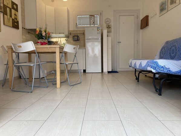 A compact kitchen with a dining table, two chairs, a sofa, and a refrigerator.