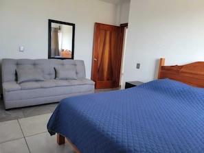 Ein Schlafzimmer mit grauem Sofa, einer Holztür und einem Bett mit blauer Bettdecke.